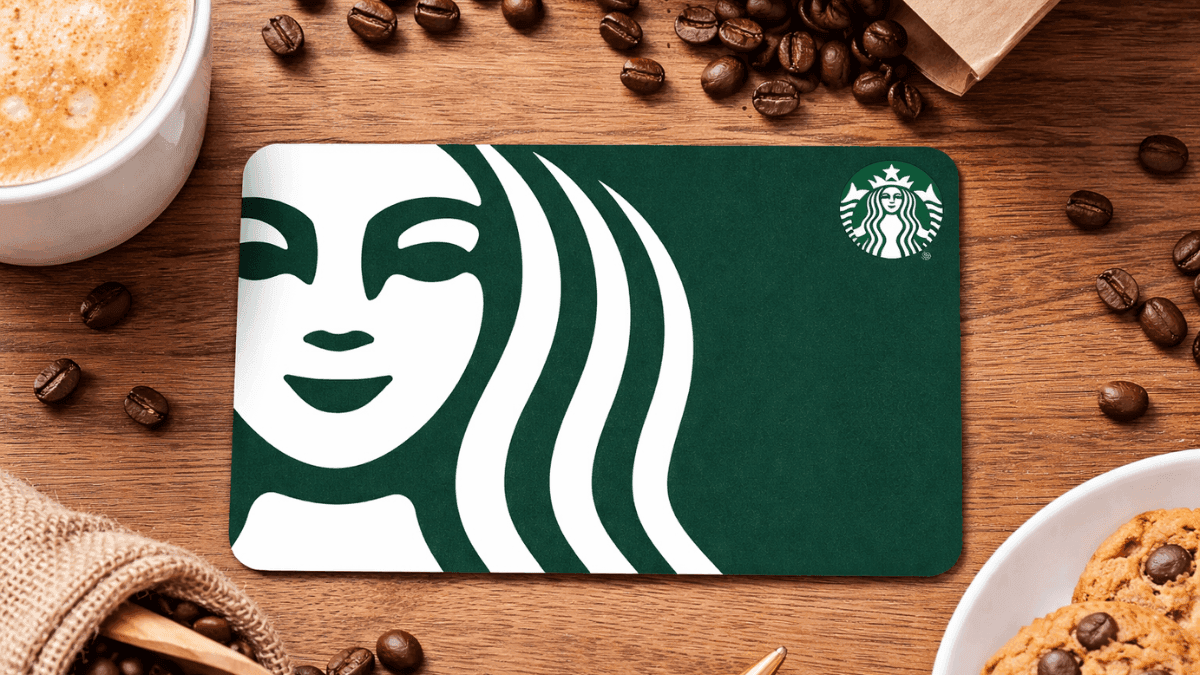 Starbucks gift card placed on a wooden table surrounded by coffee beans, a cup of coffee, and cookies.