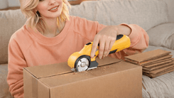 Woman using an LKCTB electric cardboard cutter to slice through a cardboard box on a sofa.